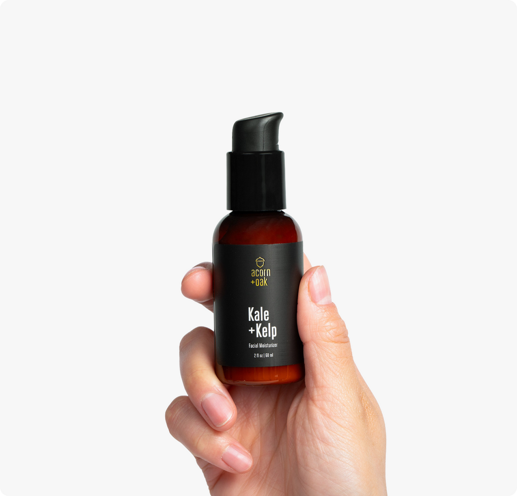 Hand holding a bottle of acorn+oak skincare product with a plain background