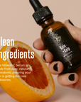 acorn+oak vitamin c serum held by a hand with an orange half in the background, text about clean ingredients.